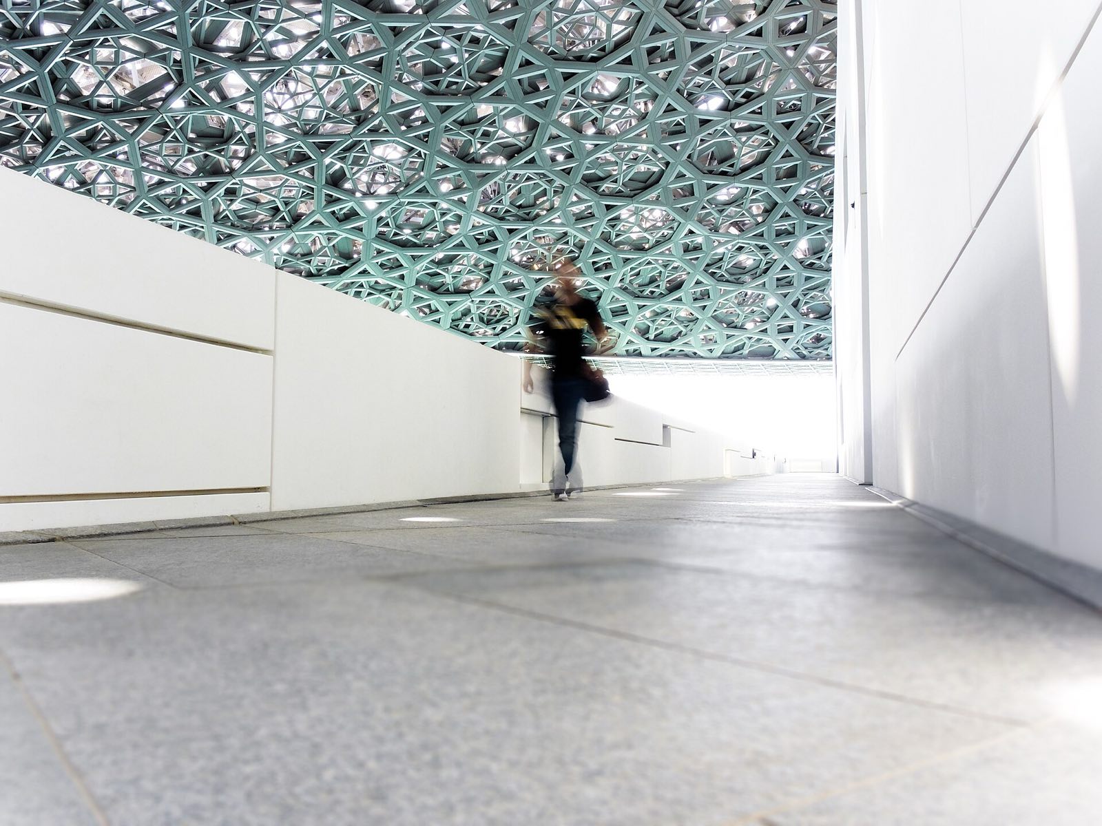 A visitor walking under the patterned dome of the Louvre Abu Dhabi.