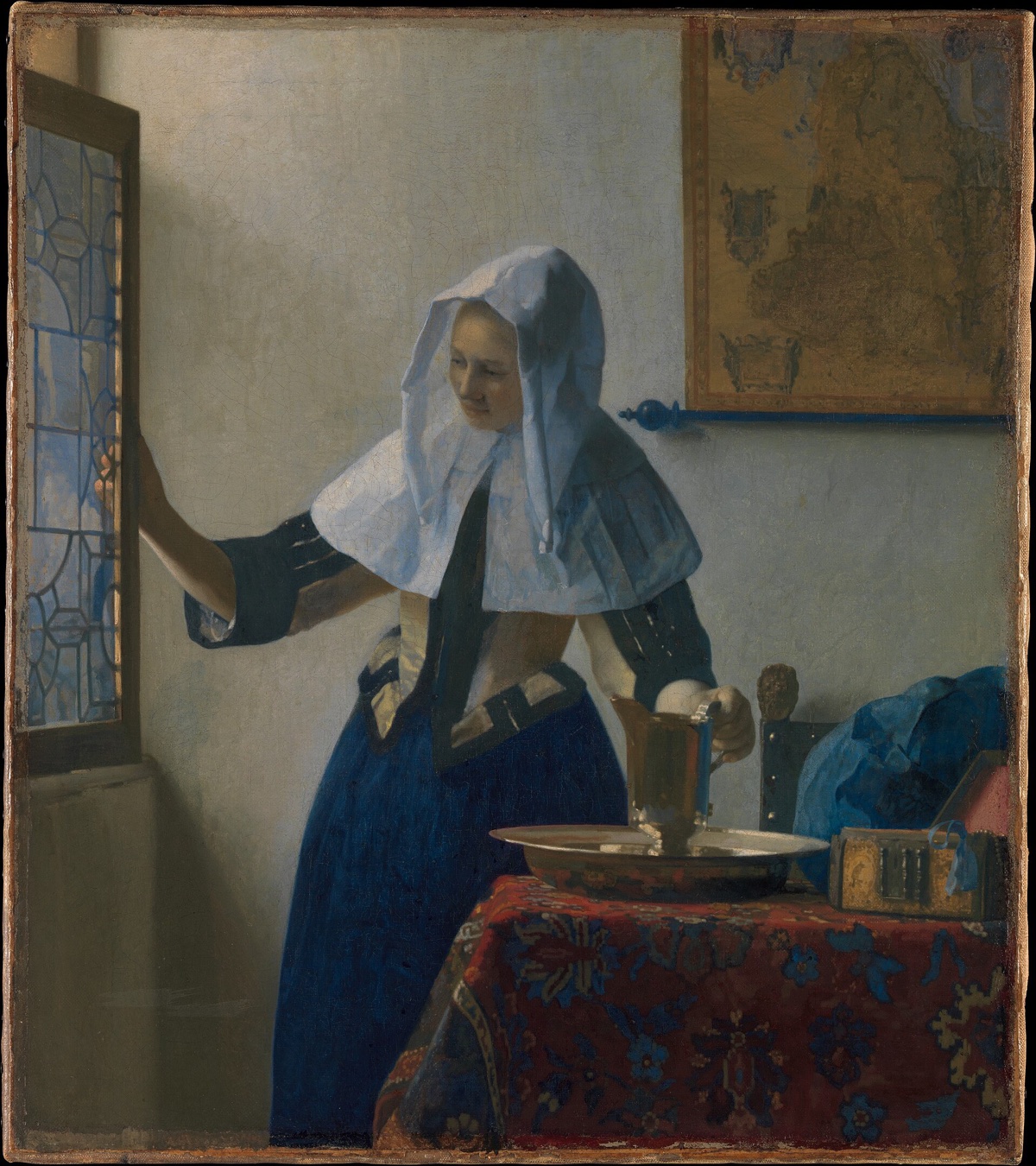 Young Woman with a Water Pitcher, by Vermeer: a woman in a white headdress opens a window with one hand and holds a silver jug with the other.