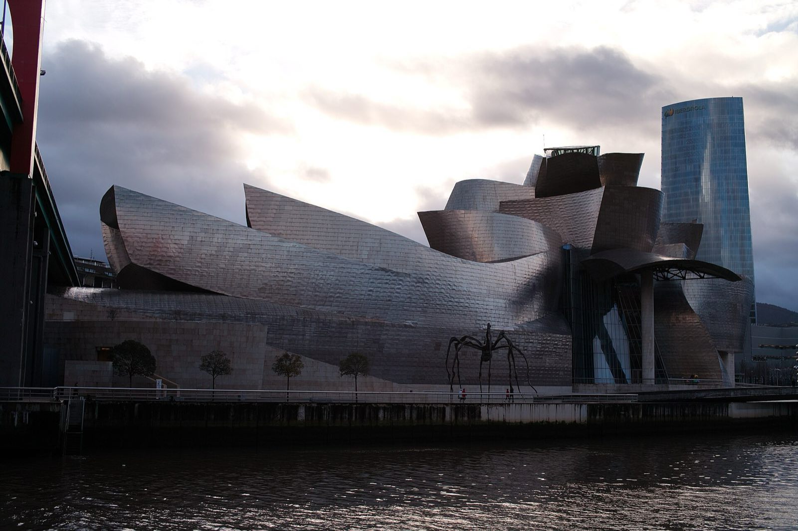 The curved titanium walls of the Guggenheim Museum Bilbao beside the river.