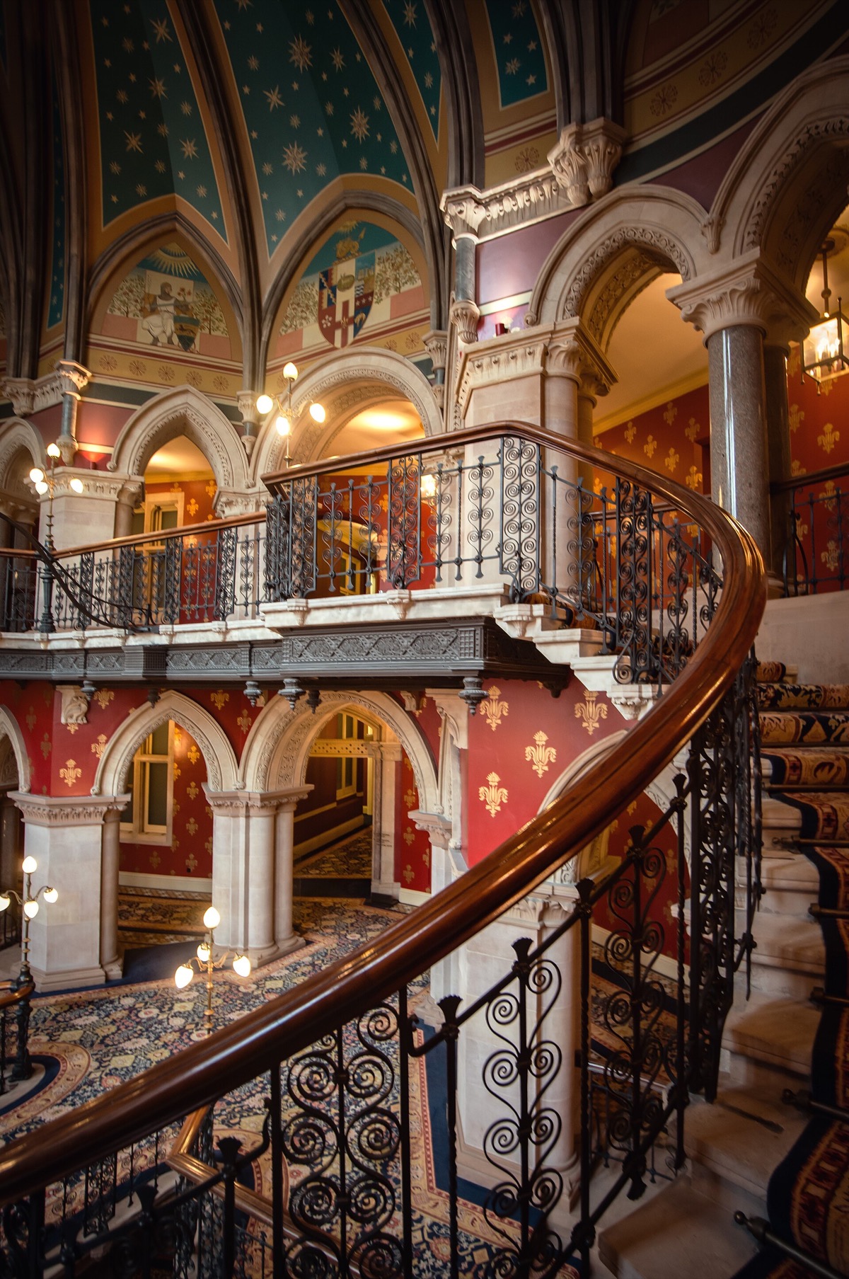 The grand staircase of the St Pancras hotel, sweeping up under painted walls and iron balustrades.