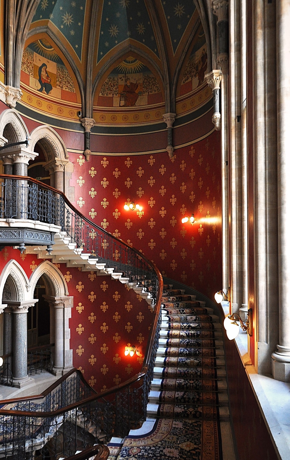 The grand staircase of the St Pancras hotel seen from below, with its red carpet and vaulted ceiling.