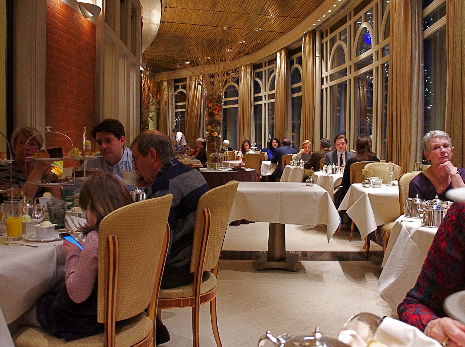 Guests at tables in a dining room of the Connaught, with tall windows onto the street.