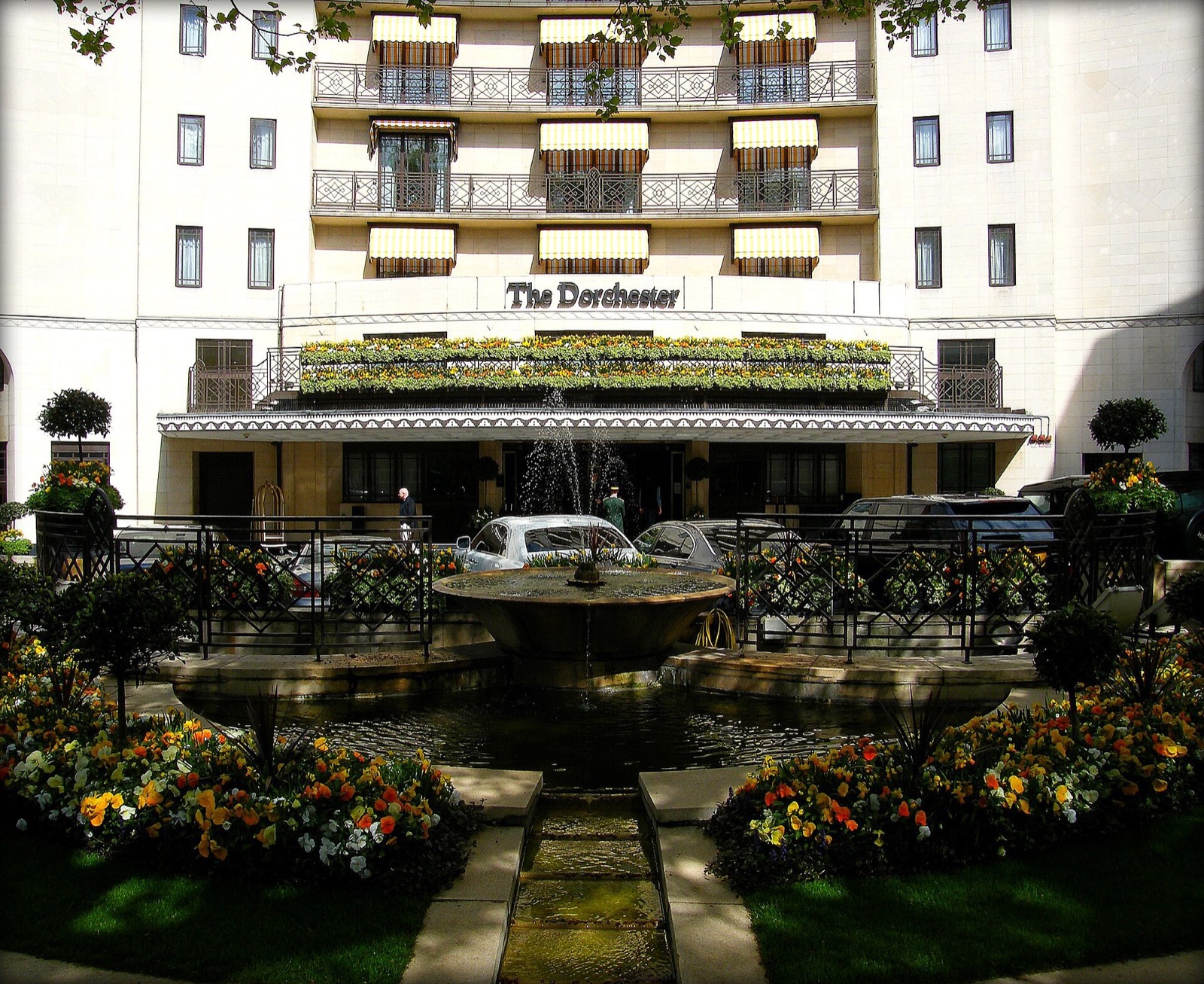 The forecourt of the Dorchester, with a fountain and flower beds in front of the entrance.
