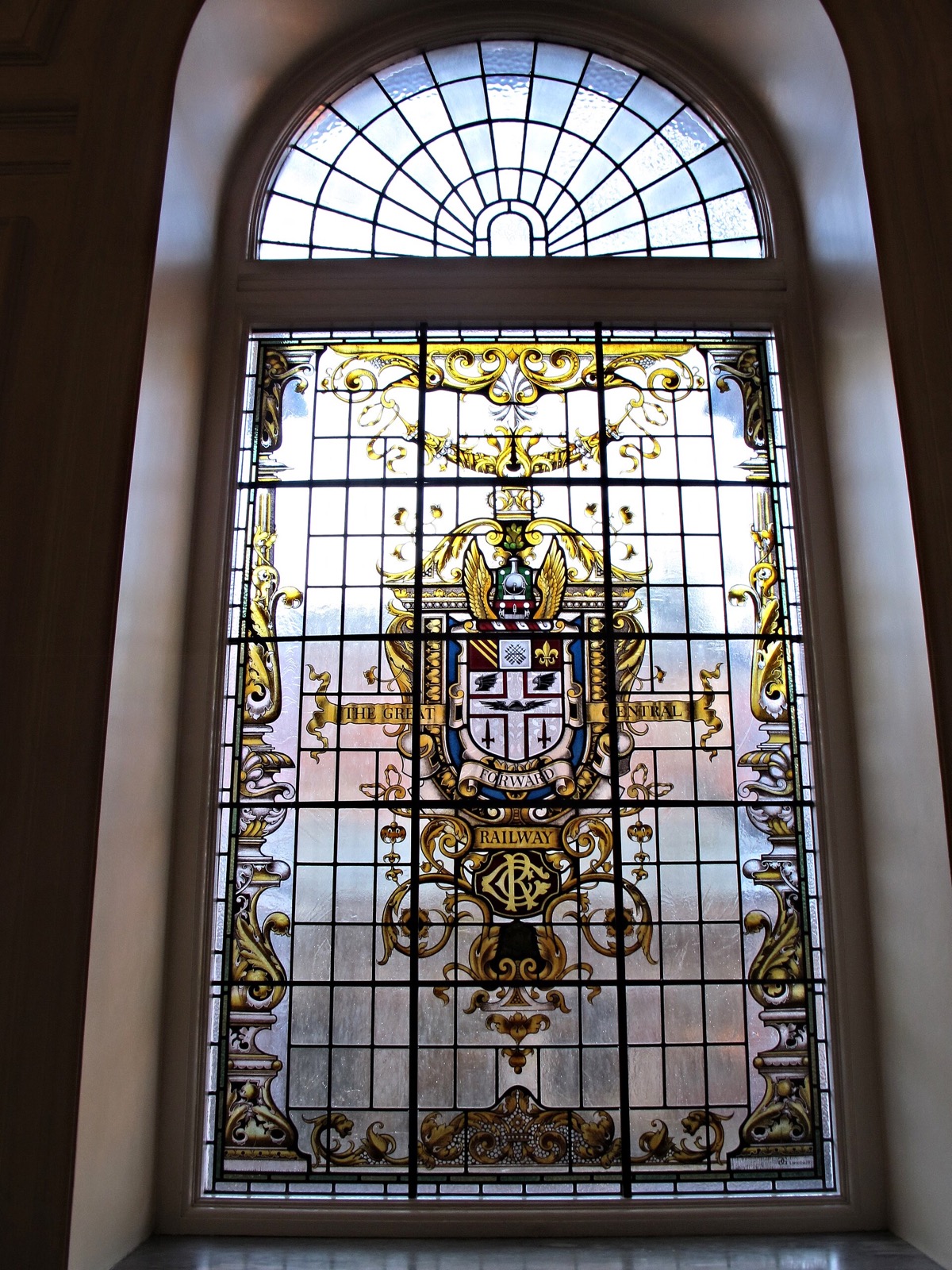 A stained-glass window of the old Hotel Great Central, now the Landmark London, with a small steam engine at its centre.
