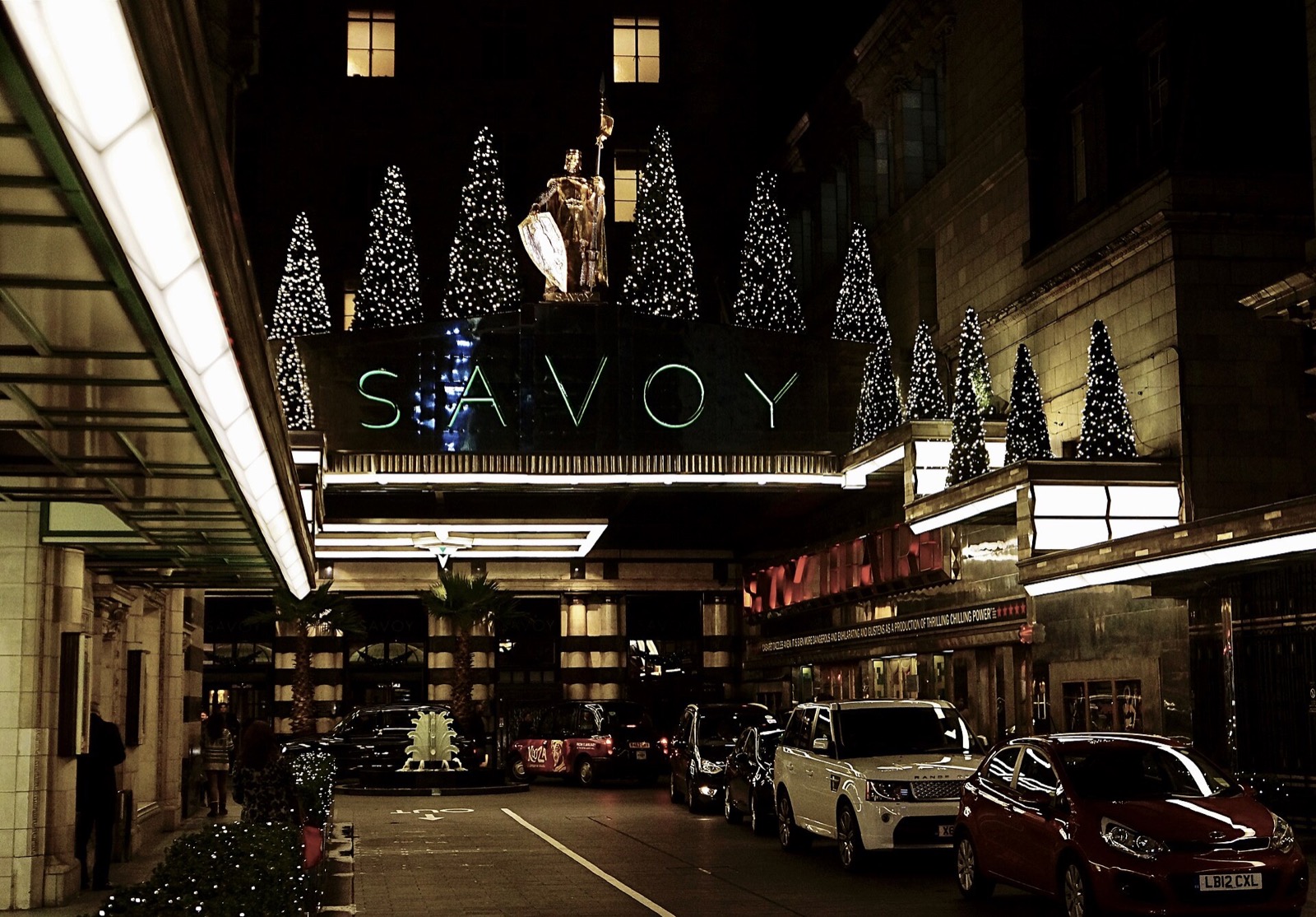 The entrance of the Savoy lit at night, with cars waiting in the court.