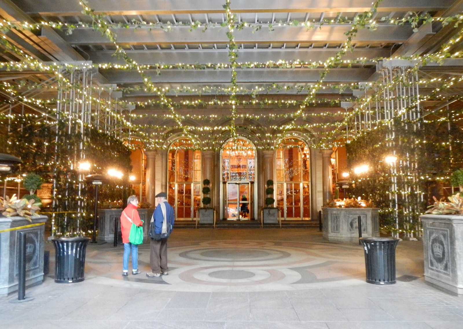 The forecourt of the New York Palace hung with lights, with the door of the Villard Houses beyond.
