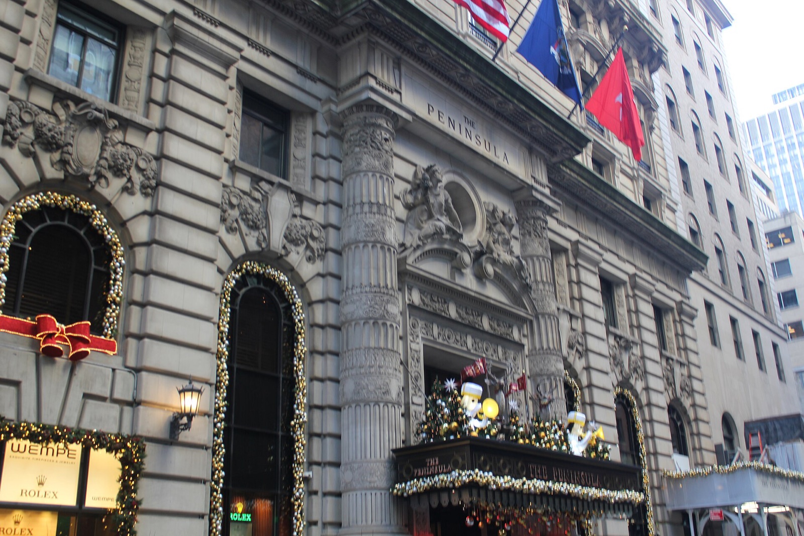 The entrance of the Peninsula New York, with flags above the door and carved stone round the windows.