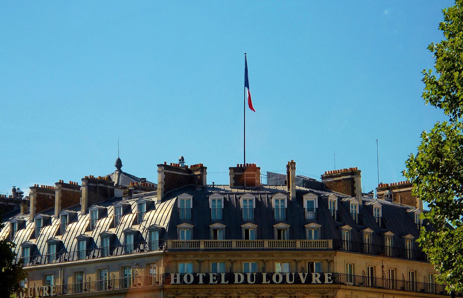 The roof of the Hôtel du Louvre with its name in gold letters, under the French flag.