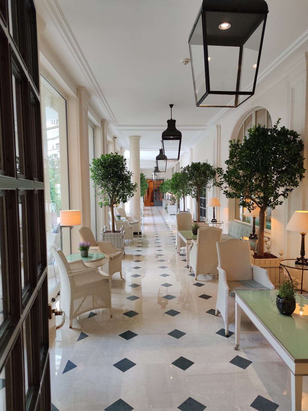 A bright gallery inside Le Bristol, with a floor of pale stone set with black, a lantern and potted trees.