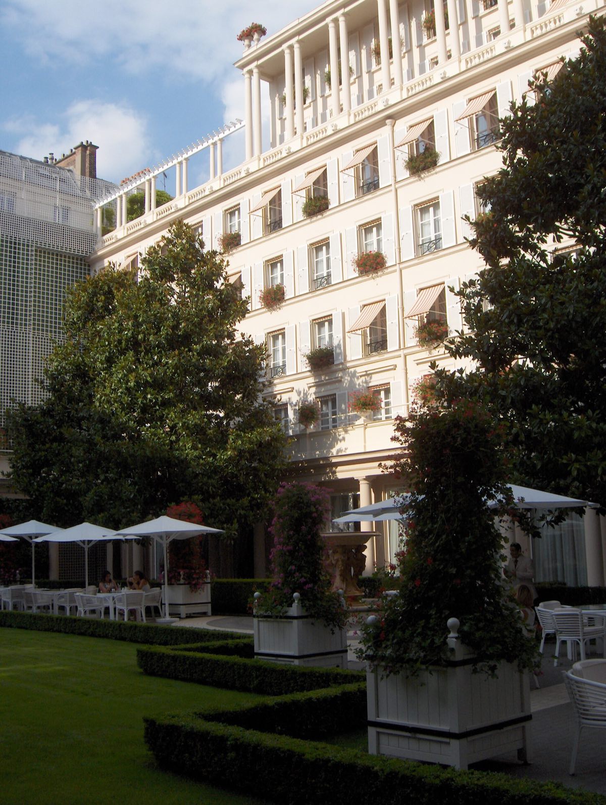 The garden of Le Bristol: a lawn, clipped trees and parasols below the white façade.