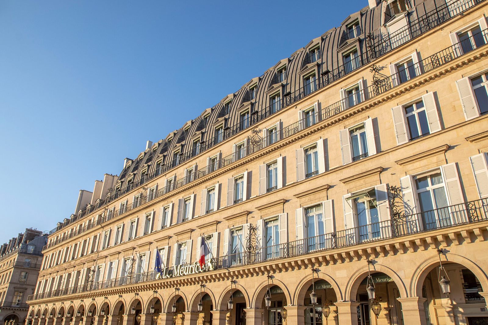The long front of Le Meurice on the rue de Rivoli, with arcades at street level, under a blue sky.