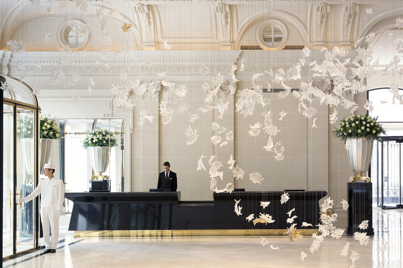 The lobby of The Peninsula Paris, white and gold, with a glass sculpture of leaves overhead.