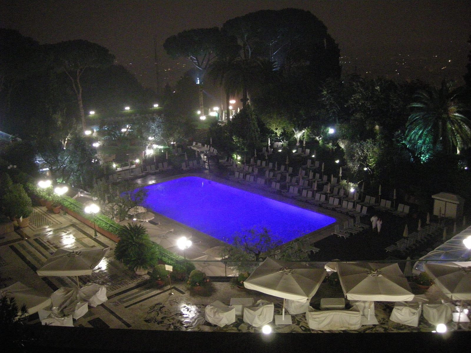 The outdoor pool of the Rome Cavalieri lit blue at night, among the trees of its park.
