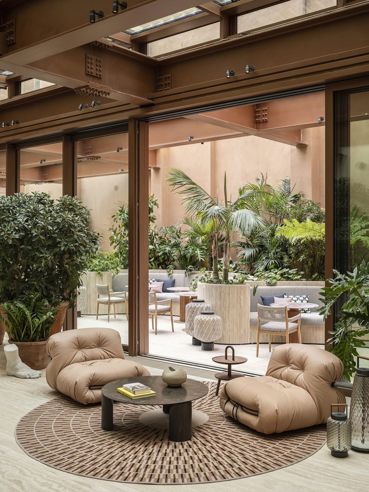A lounge of the Six Senses Rome, with low armchairs, plants and a terracotta wall.