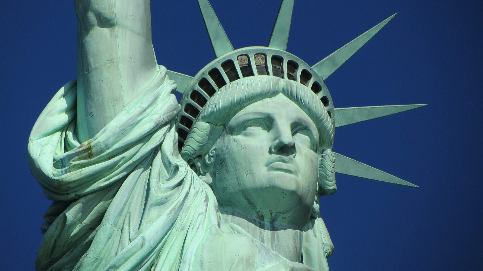 The head and crown of the Statue of Liberty against a blue sky.