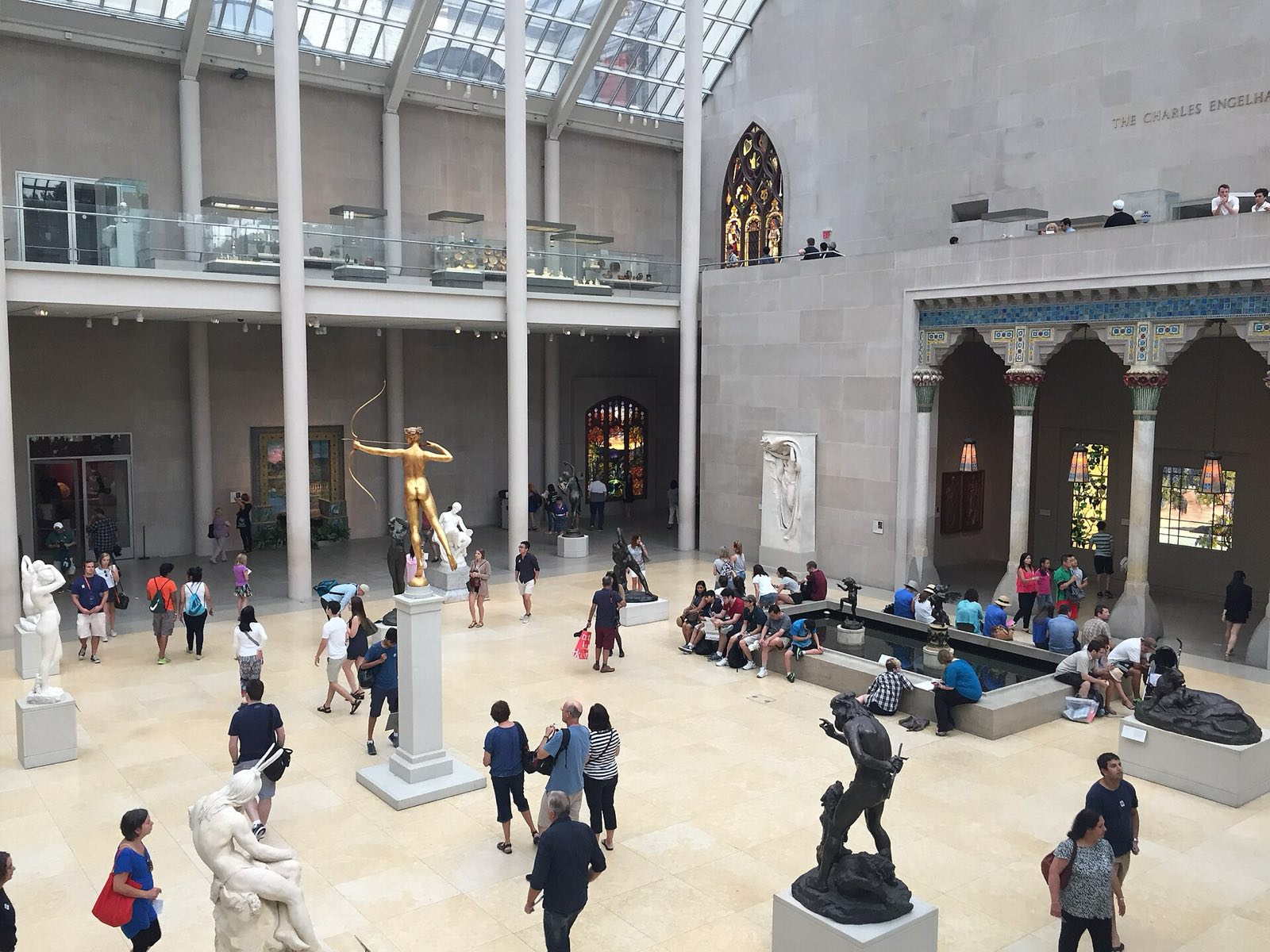 A glass-roofed sculpture court in the Metropolitan Museum of Art, with visitors among the statues.