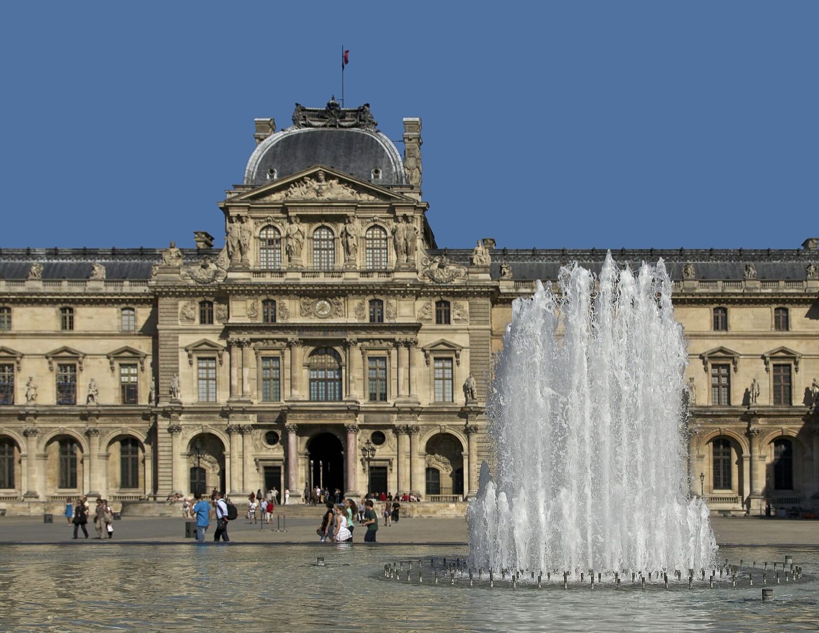 The Sully pavilion of the Louvre under a clear blue sky, with a fountain in front of it.