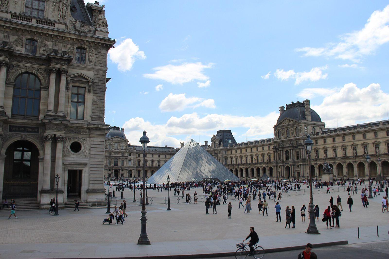 The main courtyard of the Louvre on a sunny day, with the glass pyramid among the palace wings.