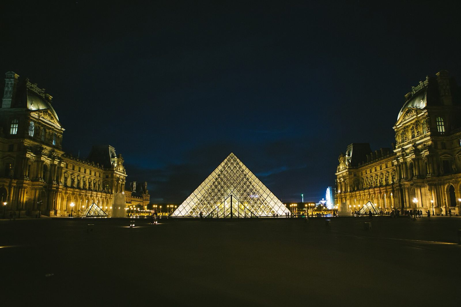 The Louvre pyramid lit at night, with the palace on either side.