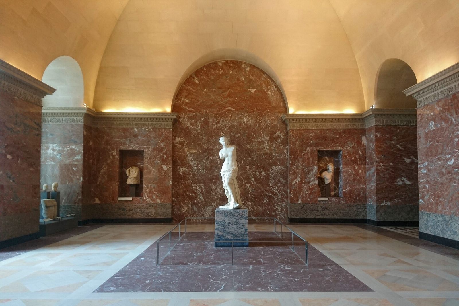 The Venus de Milo standing alone at the end of a gallery of red marble in the Louvre.