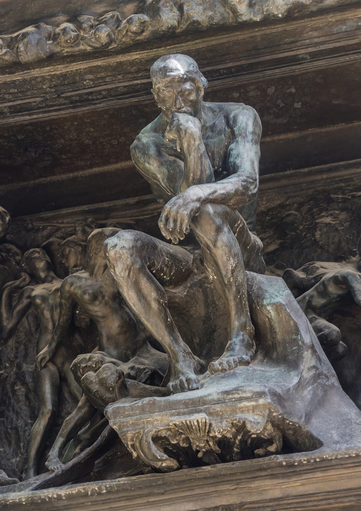 The Thinker seated above the doors of Rodin's Gates of Hell, among crowded bronze figures.