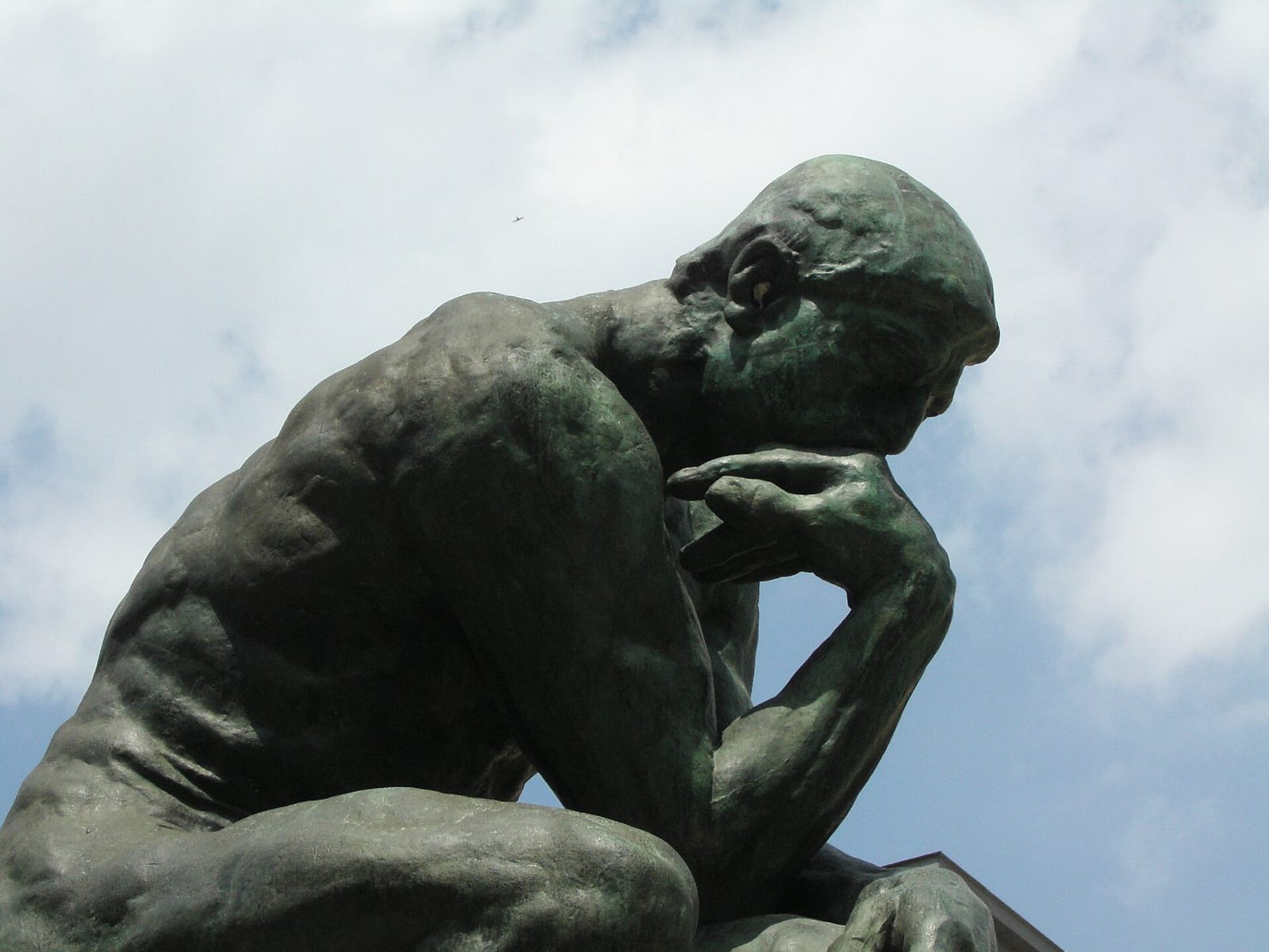 Rodin's The Thinker in bronze, seen from the side against the sky.