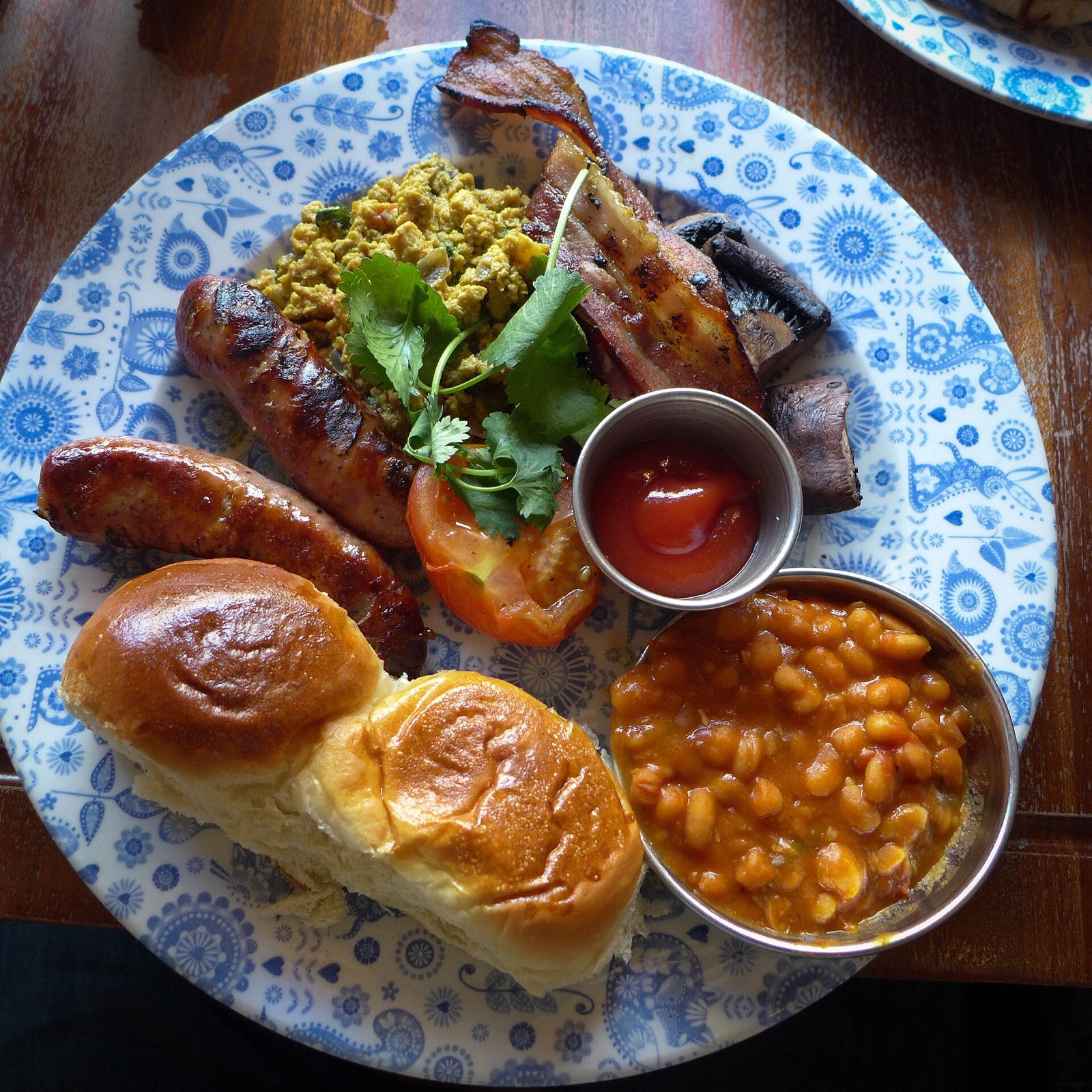 A Dishoom breakfast on a blue and white plate: sausages, beans, eggs and buns.