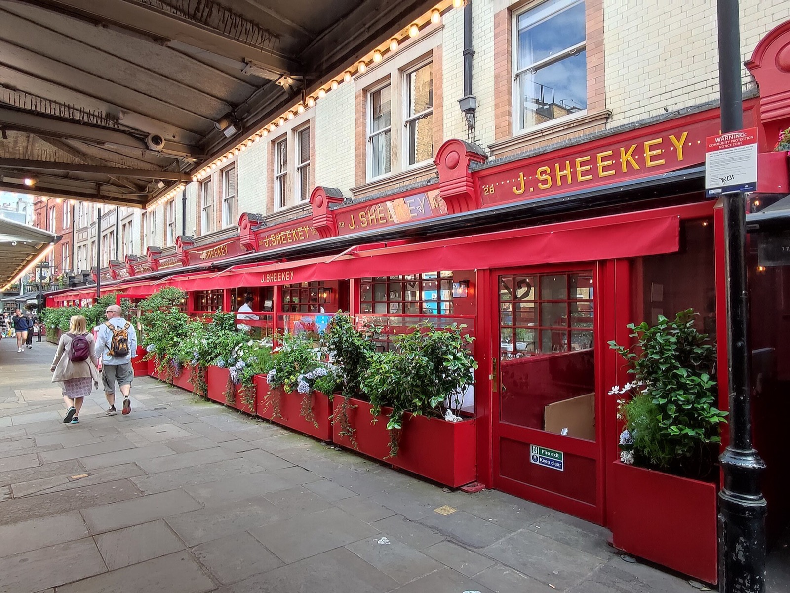 J Sheekey in St Martin's Court, a row of red shopfronts with a terrace under awnings.