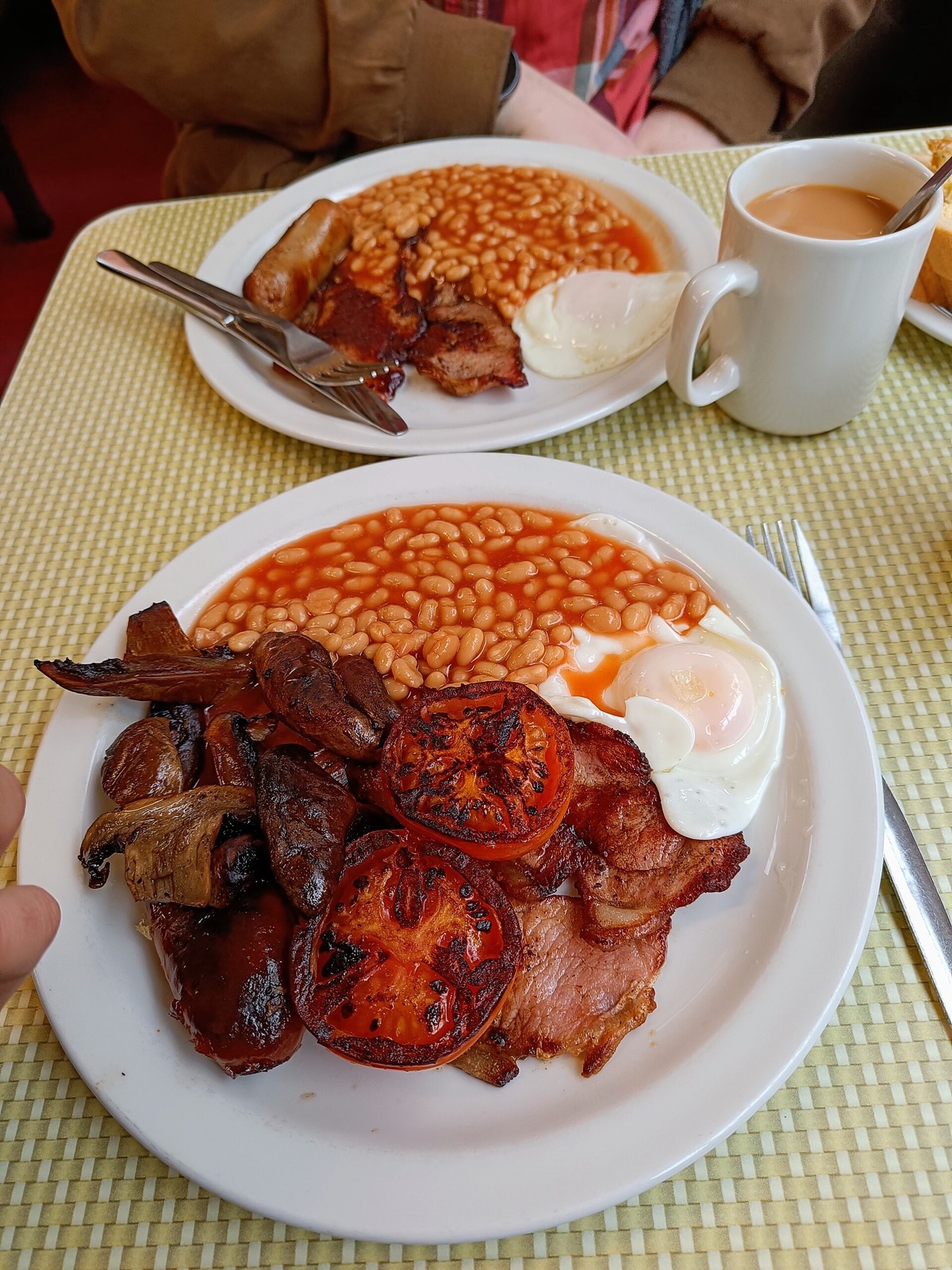 A fried breakfast of bacon, egg and beans with a mug of tea.