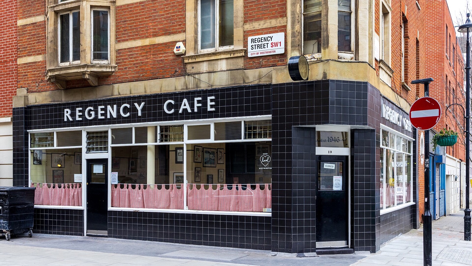 The Regency Cafe, black tiles and white lettering at the foot of a brick block of flats.