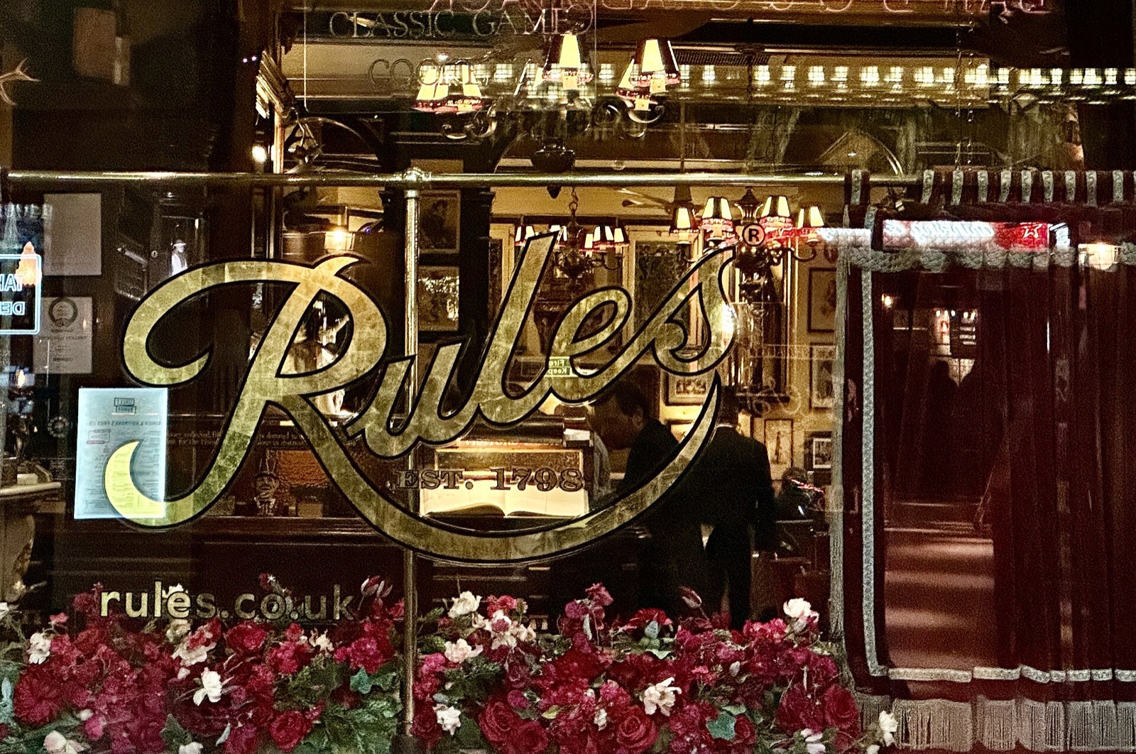 The name of Rules in gold letters on its window, lit at night.