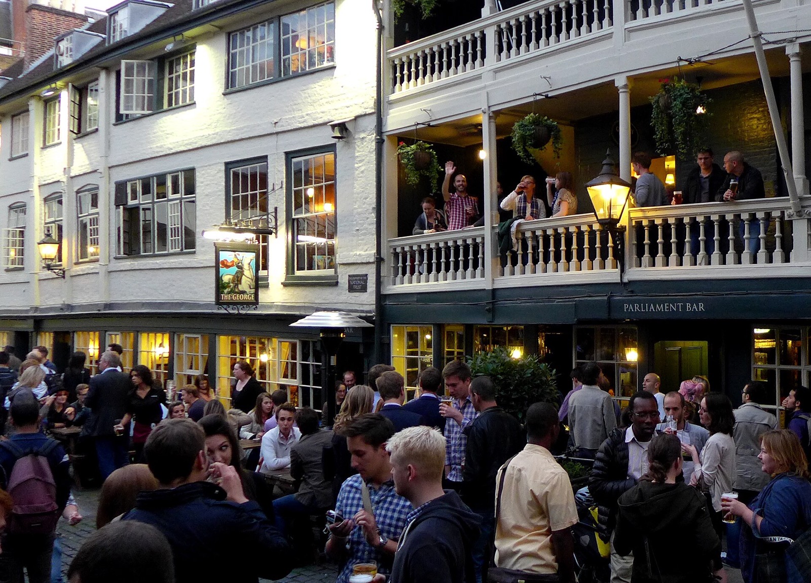 The yard of the George Inn full of drinkers on a summer evening.