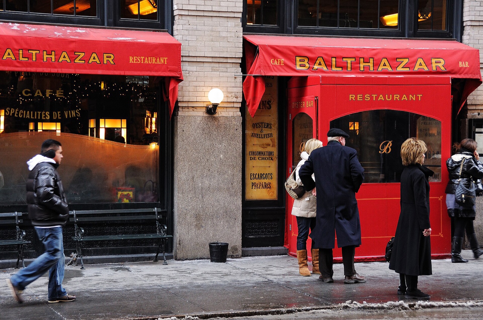 The front of Balthazar on Spring Street, with red awnings and people at the door.
