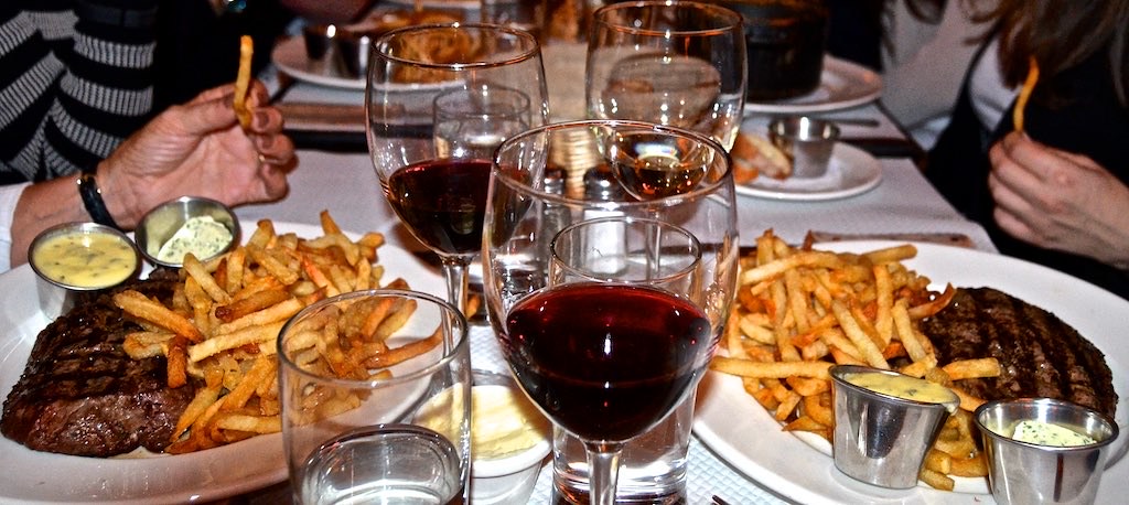 Steak and chips with glasses of red wine on a table at Balthazar.