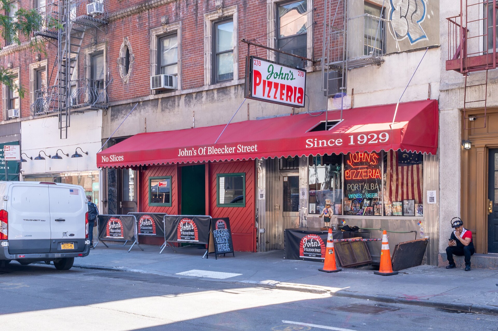John's of Bleecker Street, a pizzeria with a red awning on the ground floor of a brick tenement.