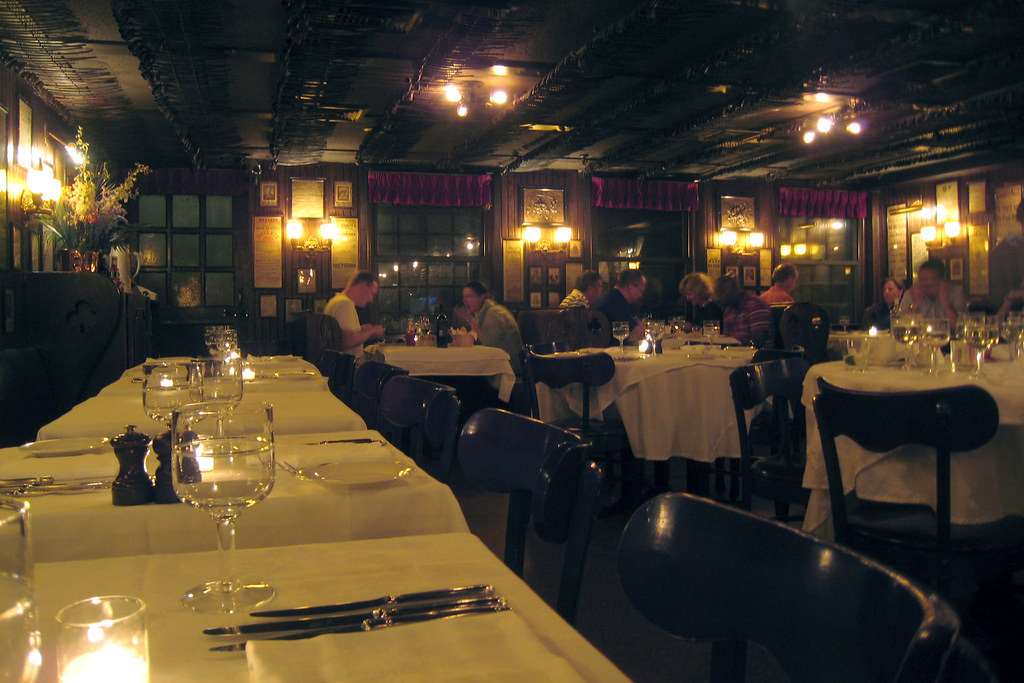 A dining room at Keens Steakhouse by lamplight, its ceiling lined with pipes.
