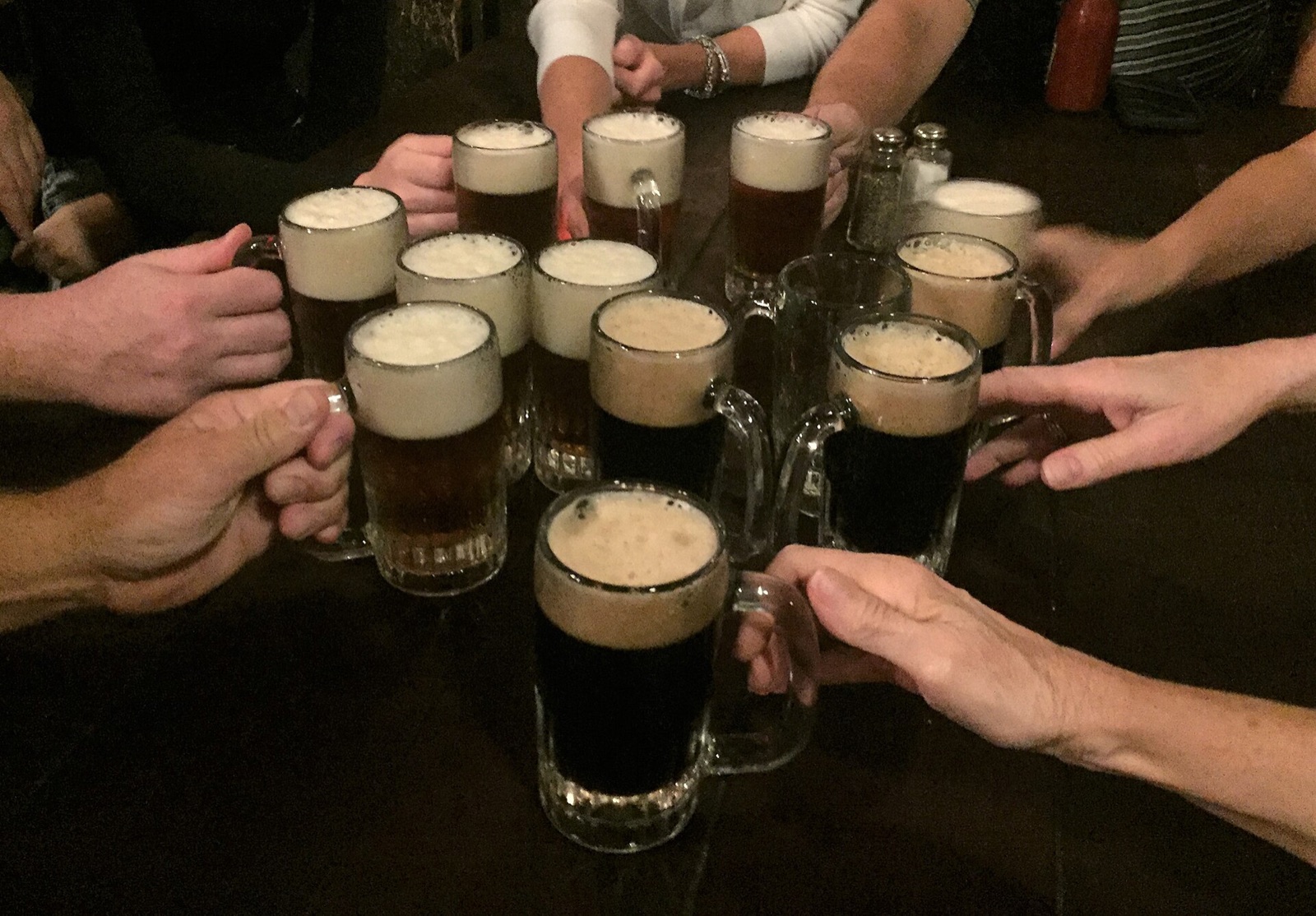 Hands raising small mugs of light and dark ale at McSorley's.