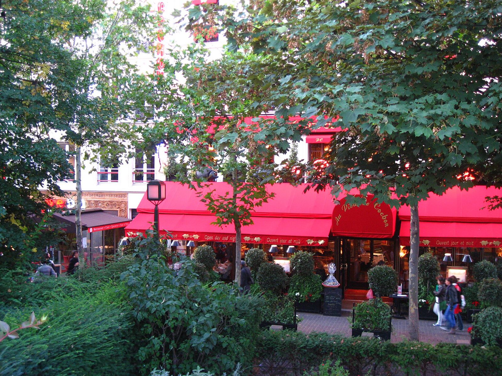 The red awnings of the terrace of Au Pied de Cochon behind a hedge.