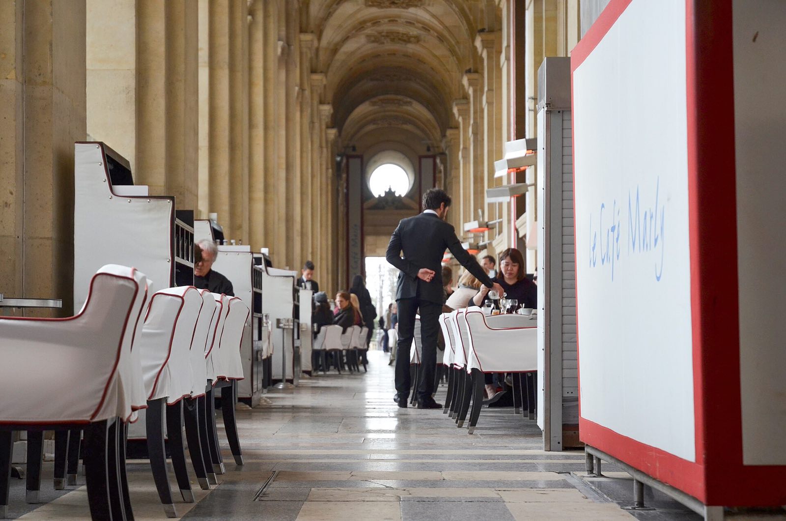 Tables of the Café Marly along the stone gallery of the Richelieu wing of the Louvre.