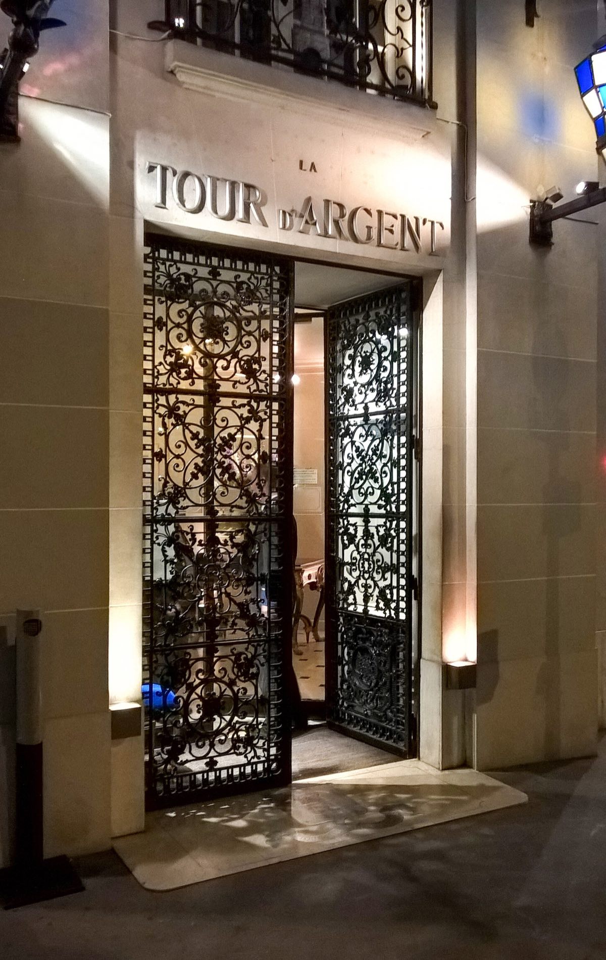 The entrance of La Tour d'Argent at night, an iron and glass door lit from inside.