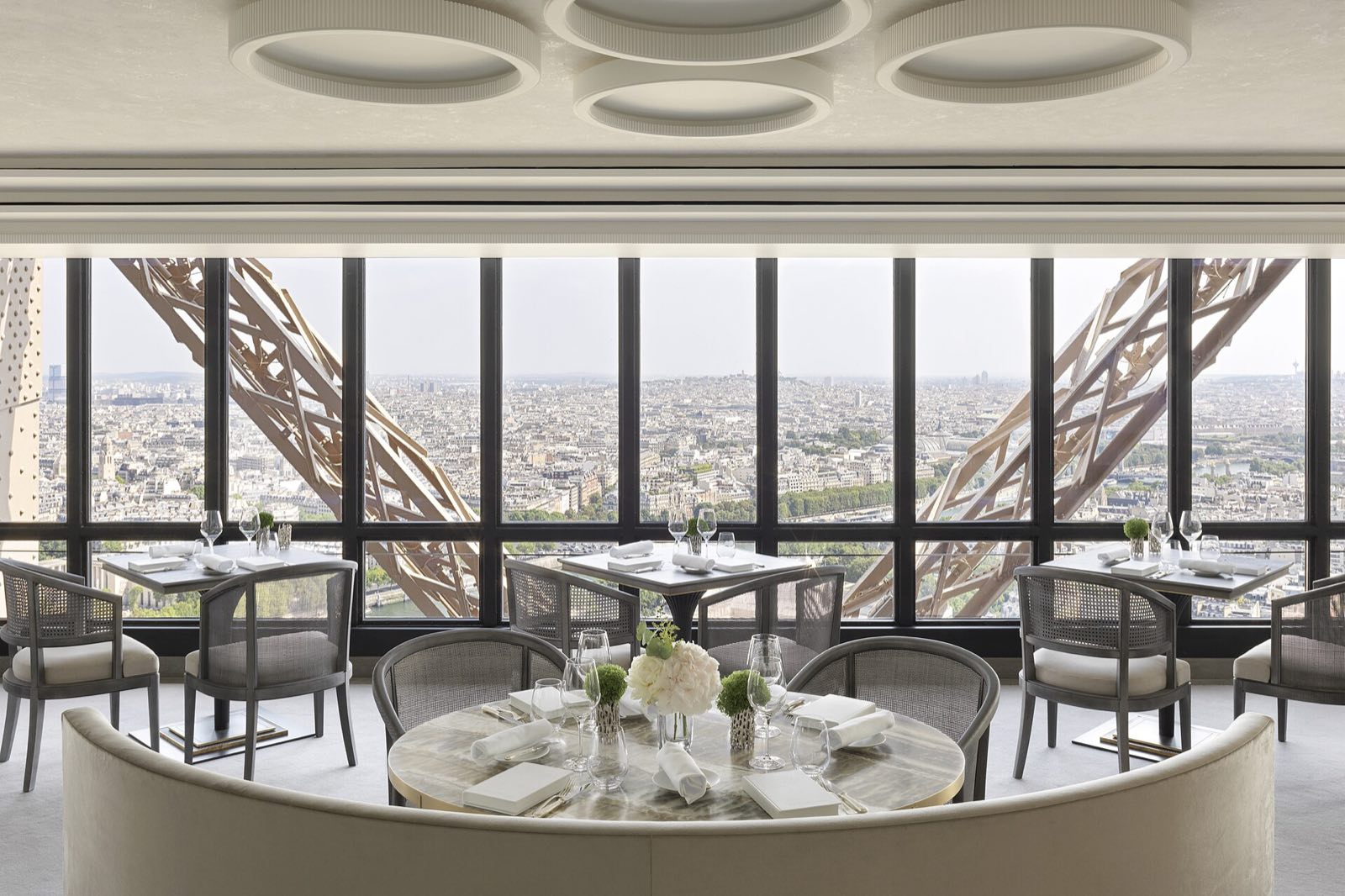 A dining room of Le Jules Verne, tables by windows crossed by the iron girders of the Eiffel Tower.
