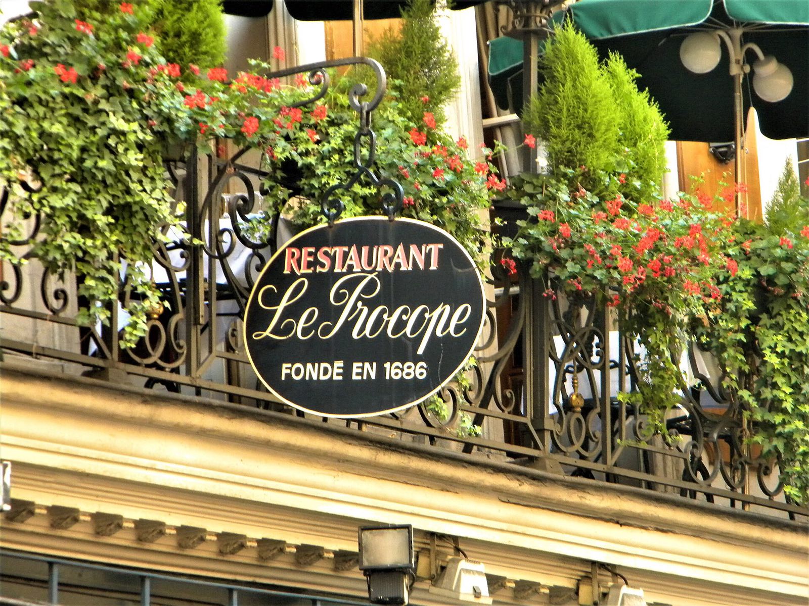 The sign of the restaurant Le Procope among the plants of its balcony.