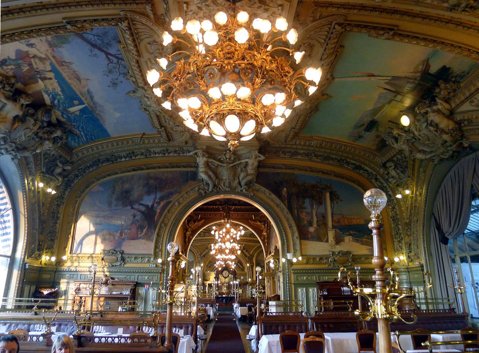 The dining room of Le Train Bleu in the Gare de Lyon, gilded arches, paintings and chandeliers over the tables.