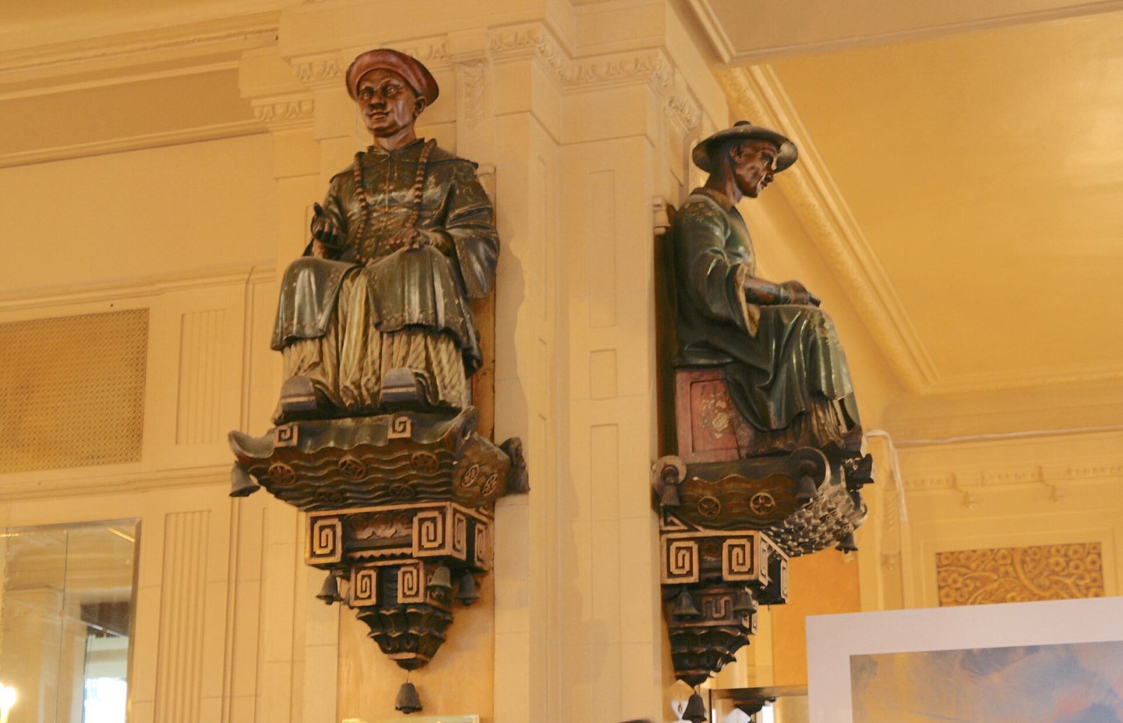 The two painted wooden figures of Chinese merchants on a pillar inside Les Deux Magots.