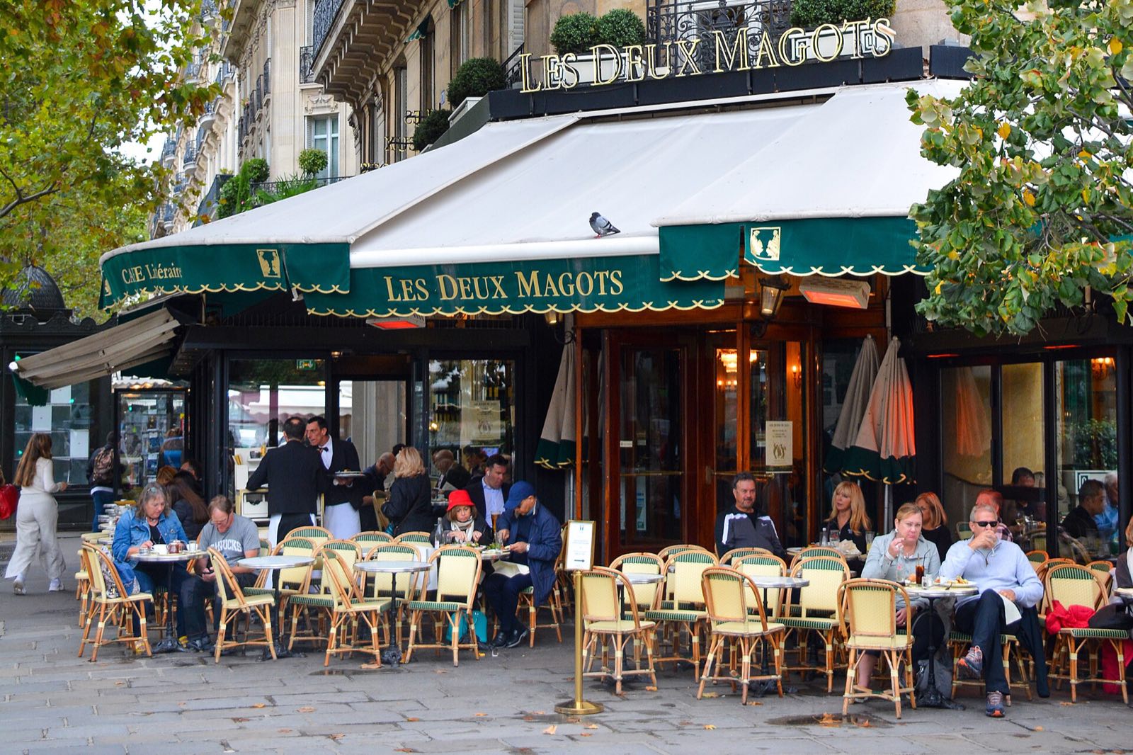 The terrace of Les Deux Magots on the Place Saint-Germain-des-Prés, full of people under green awnings.