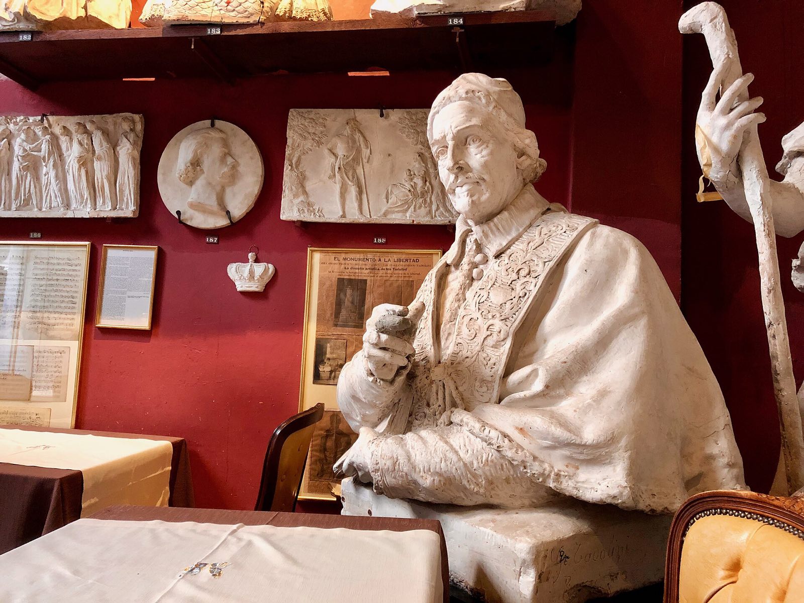 A seated marble statue among busts and reliefs on the red walls of the Canova Tadolini studio.