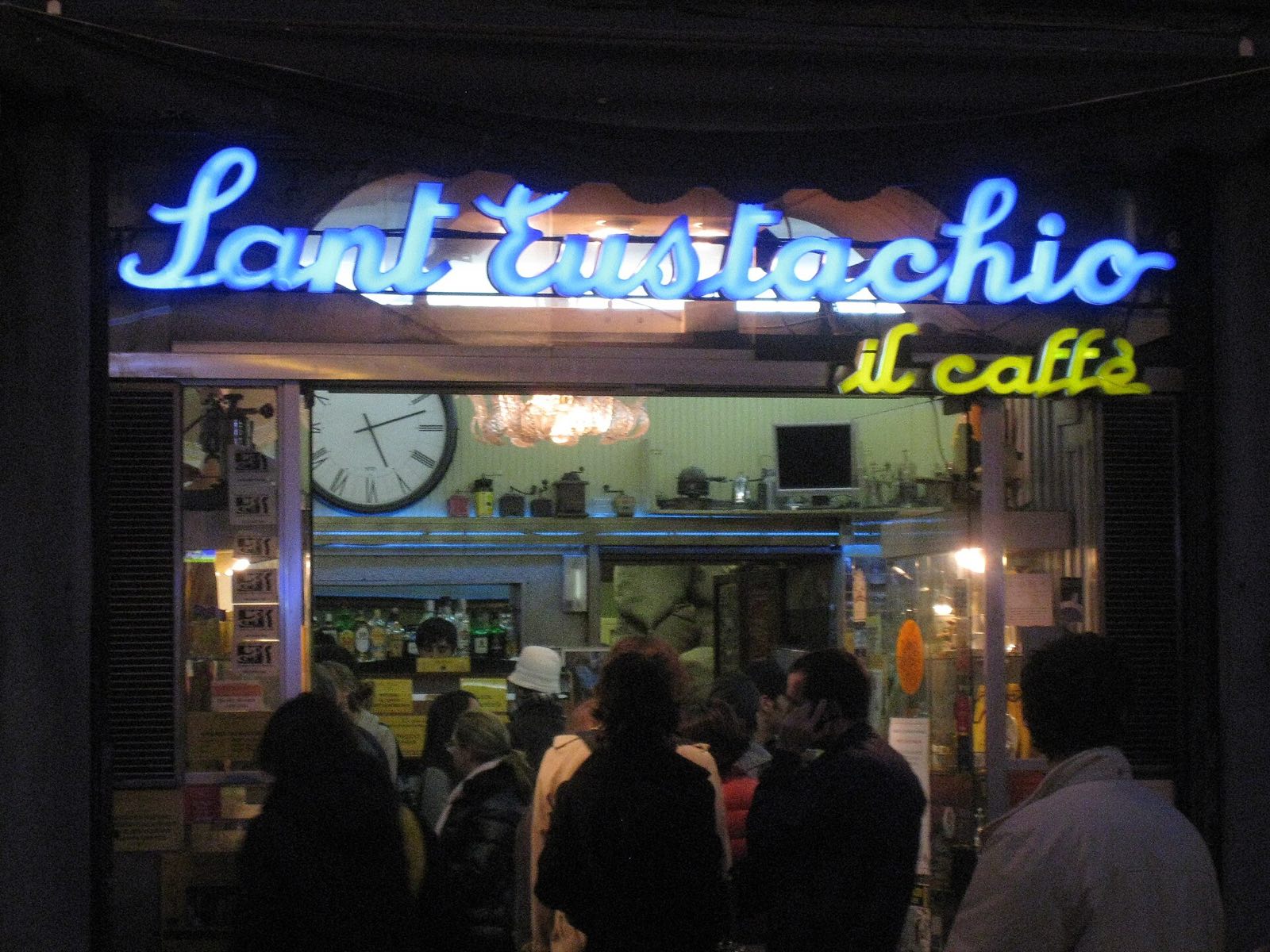 The neon sign of Sant'Eustachio Il Caffè at night, with customers at the door.