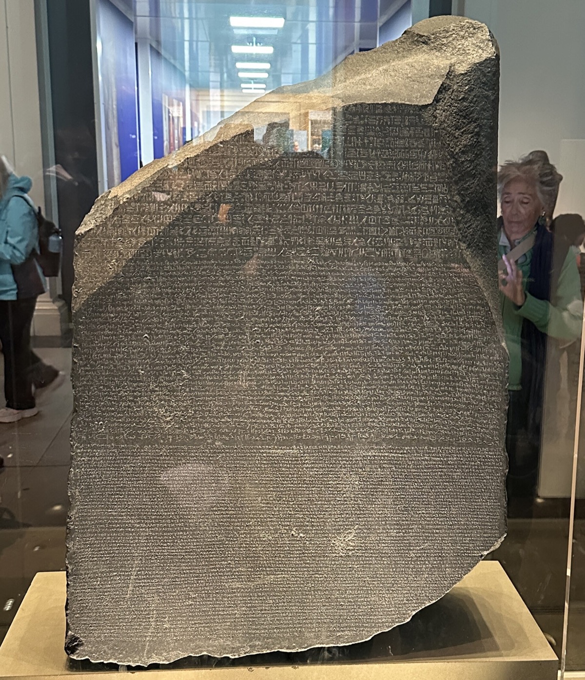 The Rosetta Stone in its case at the British Museum, a dark slab cut with three bands of writing.