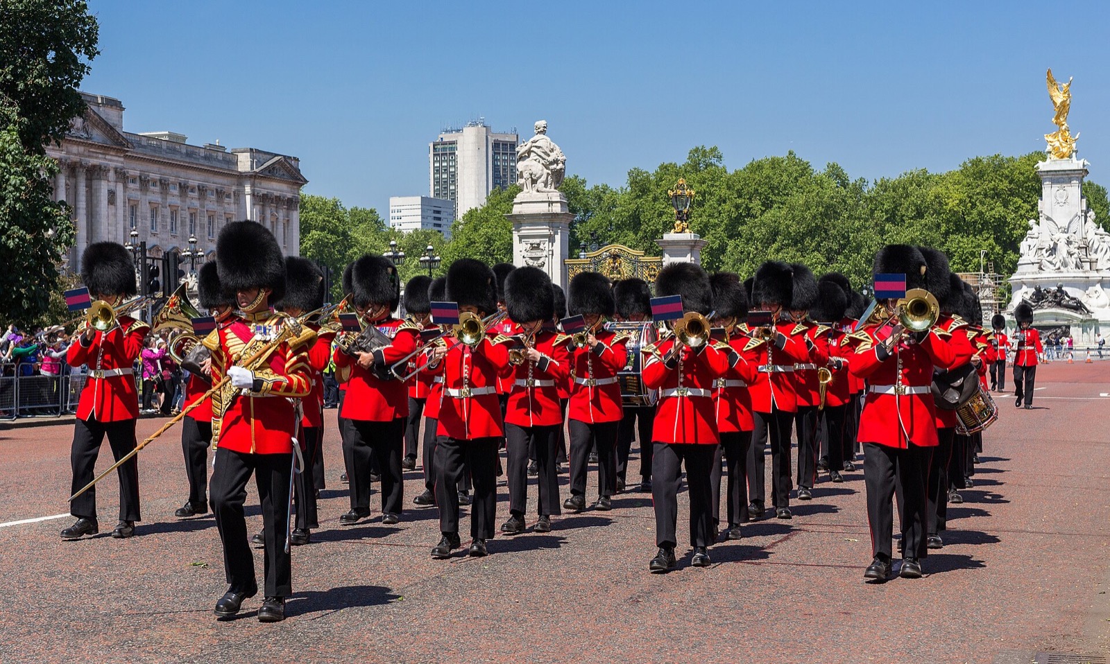 A band of the Foot Guards in red tunics and bearskins marching in front of Buckingham Palace.