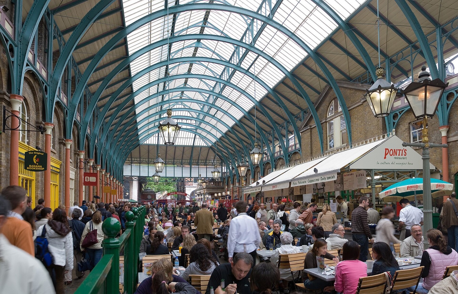 The market hall of Covent Garden, shops and café tables under an iron and glass roof.